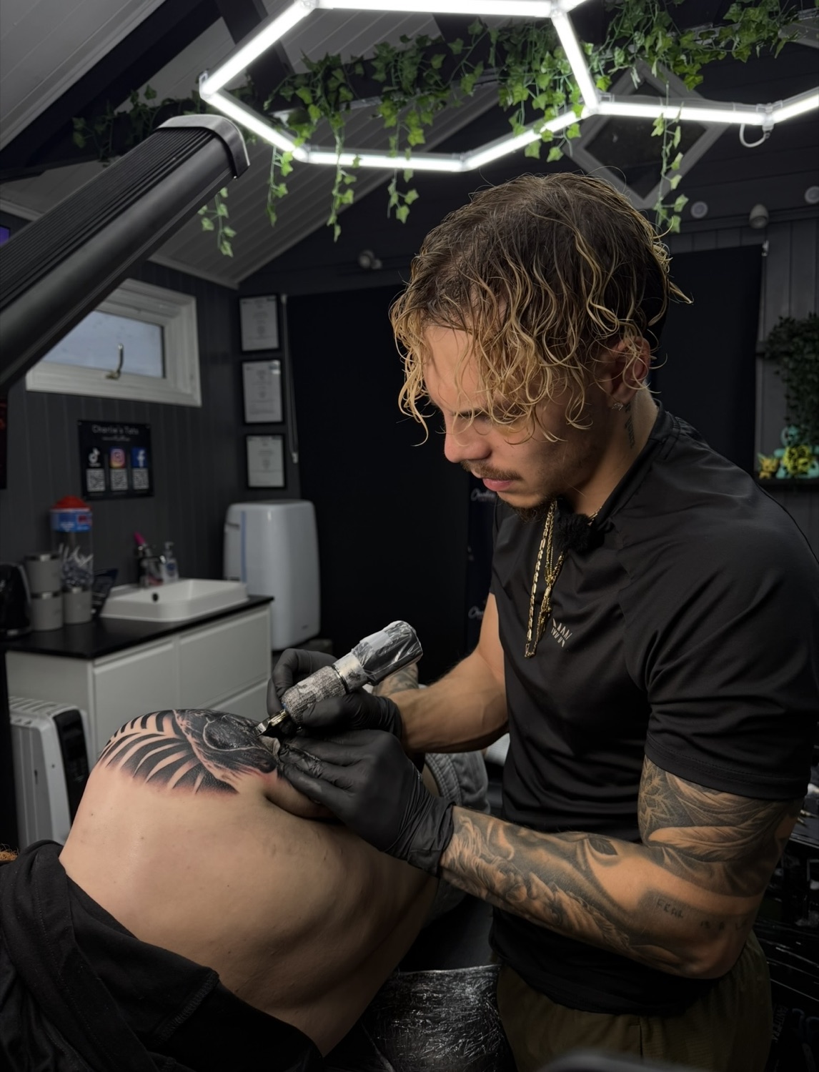 Jack tattooing a client's thigh under the studio's hexagon lights