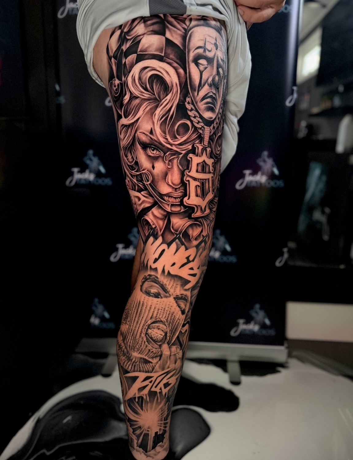 Black and grey clown faces and graffiti lettering full leg sleeve tattoo