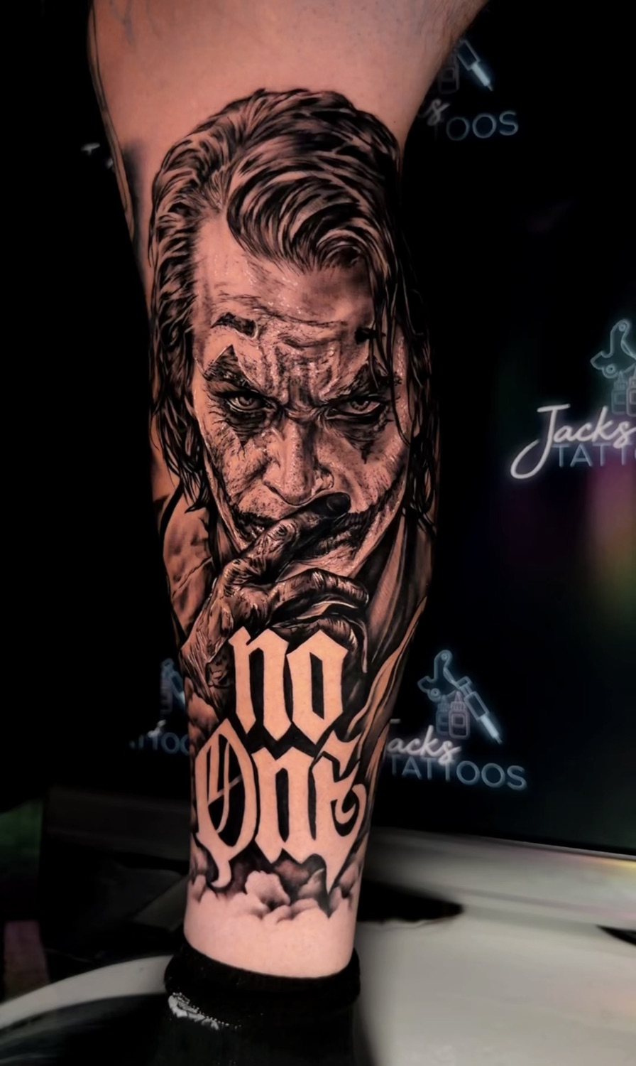 Black and grey Joker portrait with No One lettering calf tattoo