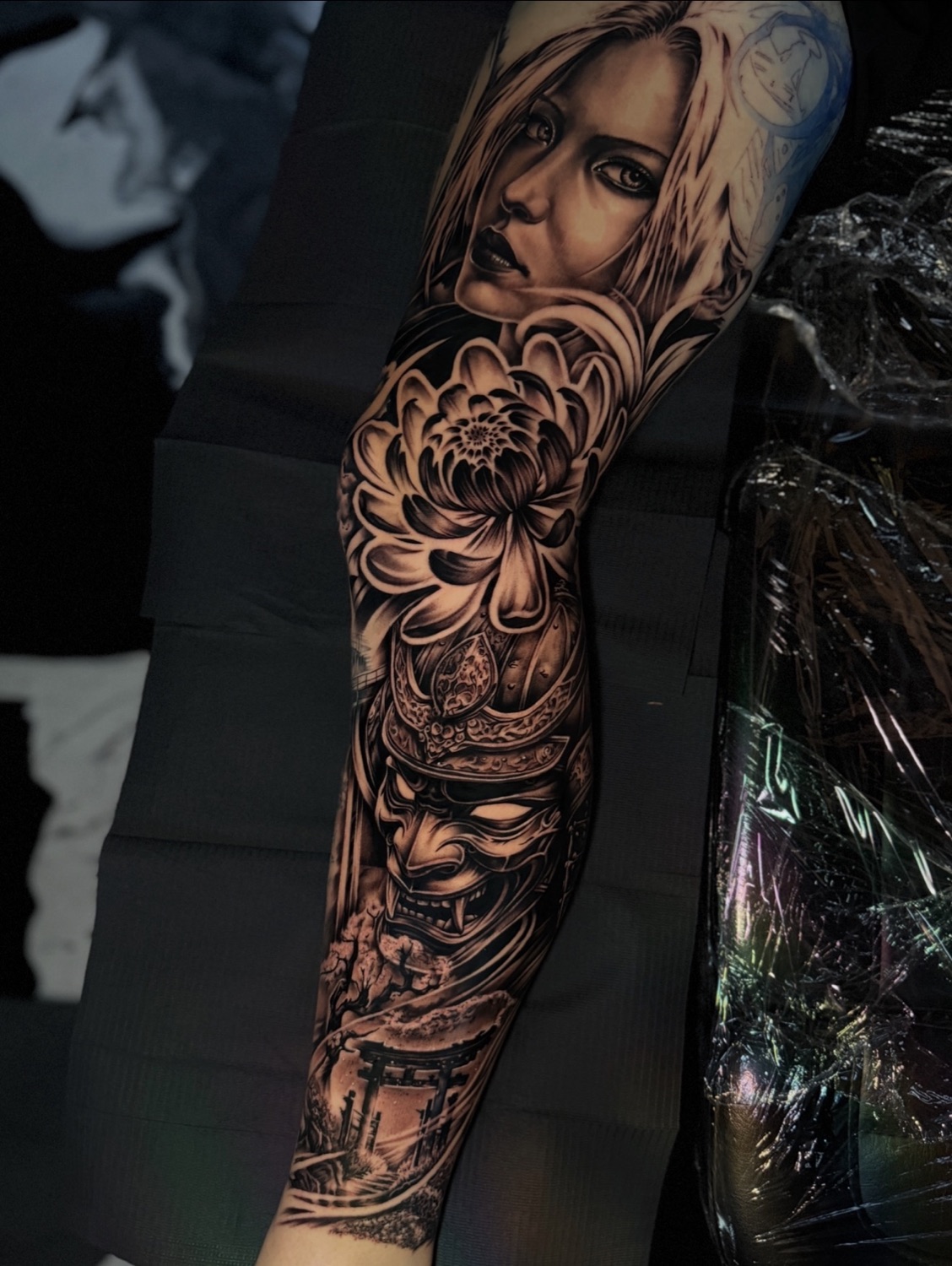 Black and grey woman portrait and chrysanthemum full sleeve tattoo, inner arm view