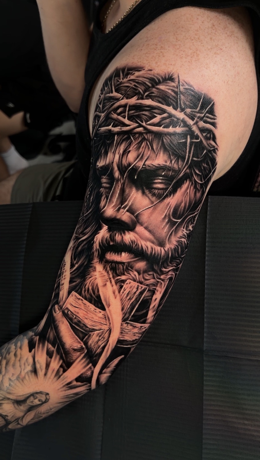 Black and grey Jesus with crown of thorns and dove upper arm tattoo
